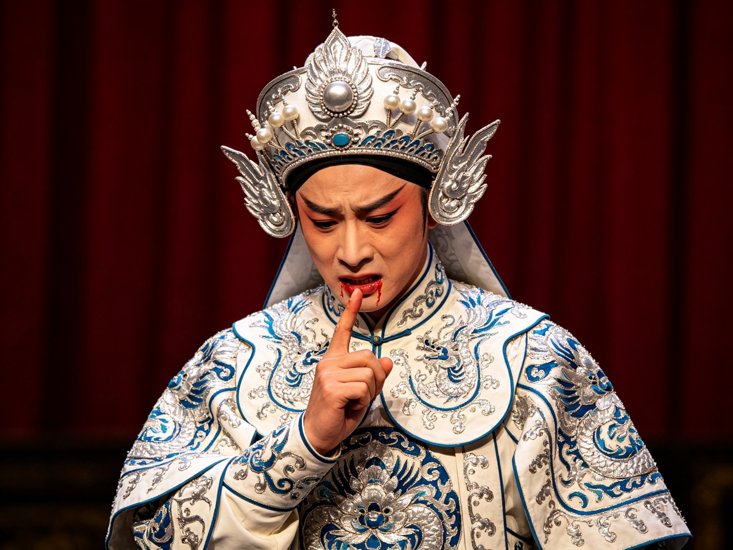 京剧《罗成叫关》叶派小生罗成扎银白硬靠、戴银白将盔，低头伸指作咬指血书状，神情悲愤苍劲