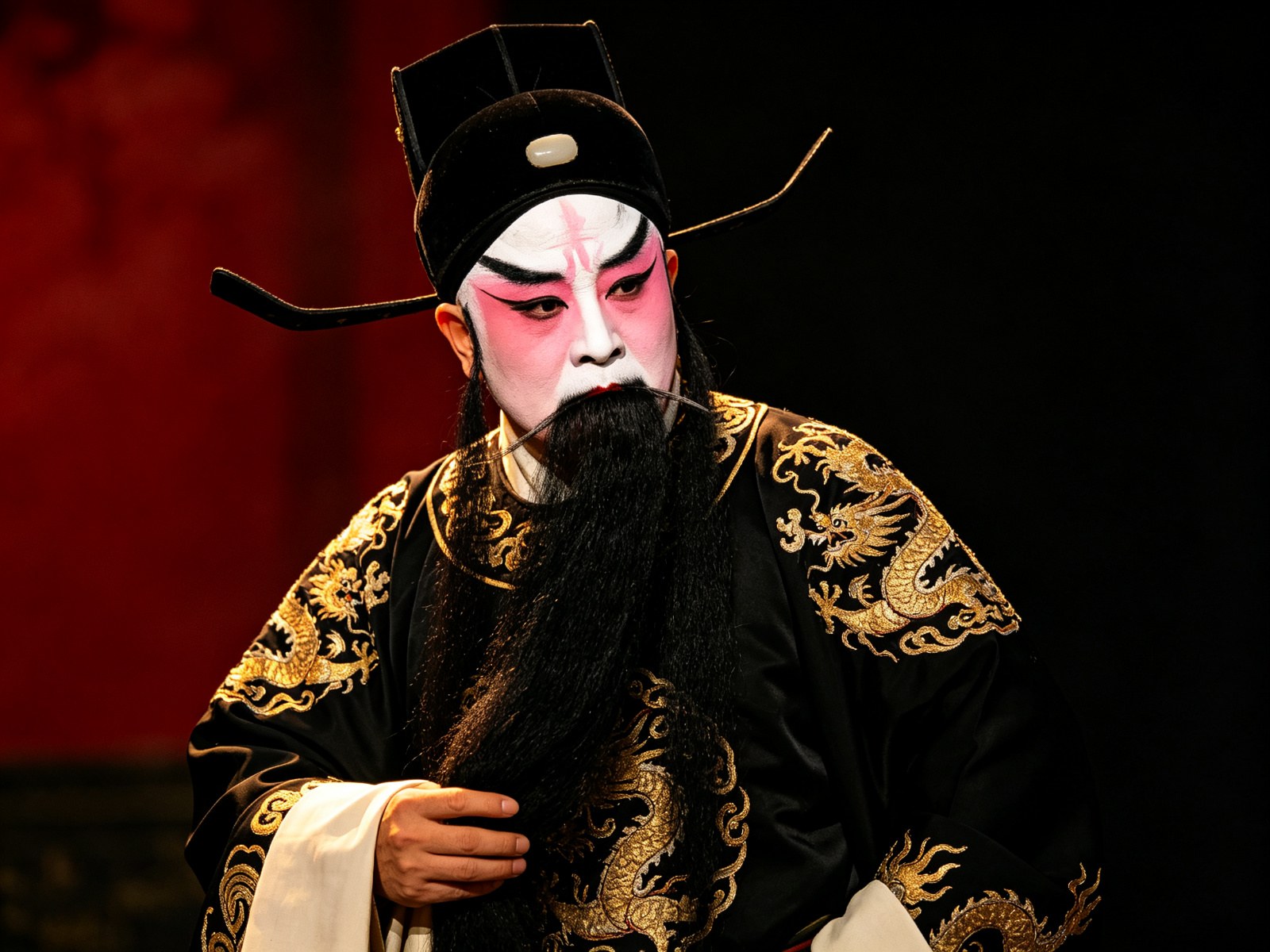 京剧《战宛城》架子花脸曹操勾画粉白奸脸、戴黑色帅盔、身穿黑色绣金蟒袍，手捋长髯、神色踌躇骄矜
